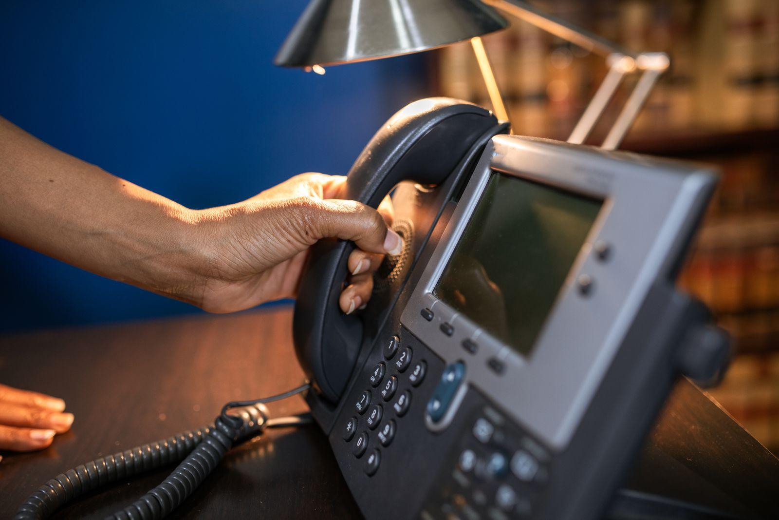 Hand lifting the handset of an office desk phone